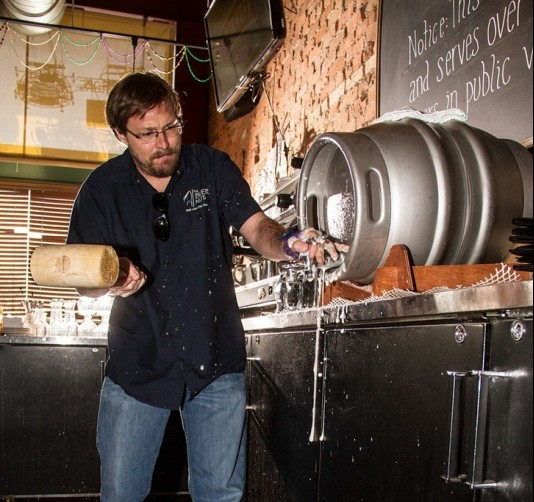 The Bayou owner Mark Alston drives a spout into a firkin cask with a wooden hammer for an entirely gravity-poured, charmingly tepid beer.