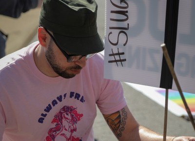 SLUG Magazine’s Lead Designer Joshua Joye decorates the magazine trolley with pink signs and hashtags. Photo: John Barkiple