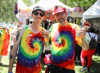 (L-R) Eric and Kevin enjoy Bud Lights at Pride. “I’m a former Mormon, and I served a mission in Richmond, VA. I think I was like 30 before I started to realize where real life was versus what I was told life actually was. I don’t believe in procreation like the Mormons preach and all that shit,” Eric said. Kevin grew up as a Catholic. “My parents always told me that this was an oppressive state where the LDS church runs everything. That’s maybe true in the government, but the people here are the best people. There’s a reason that we have one of the best Pride festival in the country, right? And this is my firstPpride since I learned that I was asexual. Well, learning what it was. I’ve always known that I was asexual, I just didn’t know that it had a name. But there’s a booth here, and I didn’t know that there were other people like me. It’s been a welcoming community. Everybody’s just so great,” Kevin said. Beyond that personal experience, Kevin is impressed with the support from City Hall. “I bet there are people working this event like police officers and people from the state who might not agree with this event, but they agree that ‘We the people’ means everyone,” he said. Photo: John Barkiple
