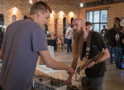 (L–R) DFX’s Brad Burnell points out features of the “F.M. Fuzz” effects pedal while Tyler Gipson takes it for a spin. Gipson plays in Esther Lane and has a solo project called Weasel Fever that’s pure metal.