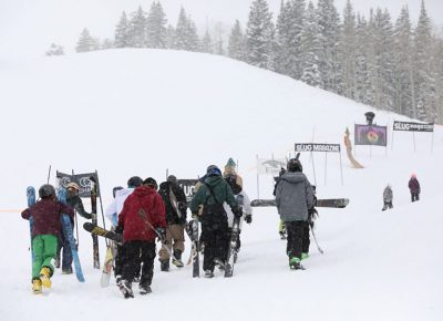 Skiers and snowboarders trek uphill.