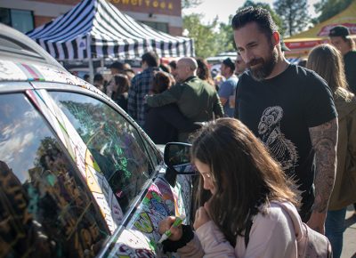 (L-R) Brian and Sosie Carlson put in some EXPO marker time on Mark Miller Subaru’s Art Car. Sosie is satisfied with her green squiggley line. Photo: John Barkiple
