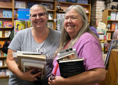 (L–R) Meg Drage and Maire Nelligan fill their arms with books. Drage, ironically, has a book on back health at the top of her heavy stack.