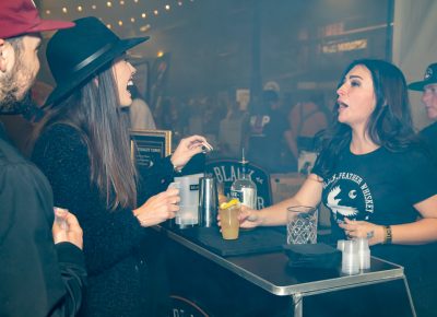 (L–R) Spencer McCann waits while Brenna Stumbras pays Olivia Bergmann for a Whiskey Tango cocktail at the Black Feather Whiskey booth.