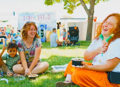 A couple of friends enjoy some shade and Cupbop while listening to the performers on stage.