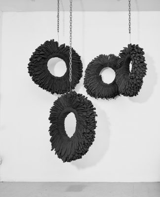 Michael Pribich, Essential, 2020. Installation with 4 wall-mounted and ceiling-suspended elements: brown cotton work gloves over rolled ¼ in. steel rods, steel chain, dimensions vary, each glove wheel 28-32 in. diameter, suspending chain lengths vary. Photo by Max Yawney. Image courtesy of the artist. 