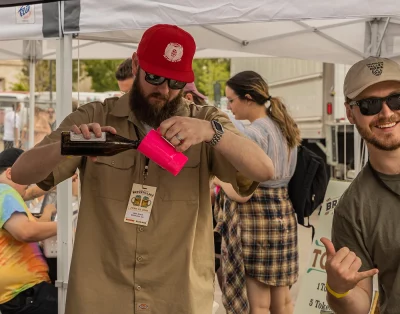 A member of the Red Rock Brewing crew pouring a cold one as an attendee comes in hot with the photo bomb!
