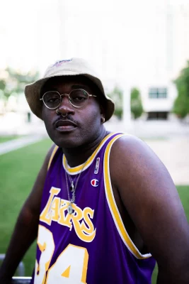 James Ray Davis III wearing a bucket hat, glasses, and a Lakers basketball jersey.