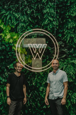 Zach Howa (L) and Ryan Reich (R) stand in front of the Woodbine logo in front of the living plant wall.