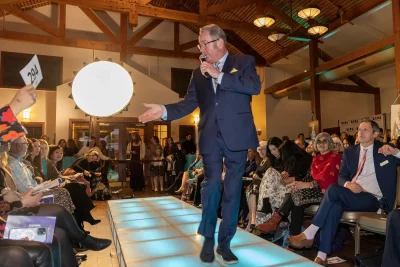 Auctioneer Larry Flynn walks the runway in search of bids for a Ponderosa Ranch getaway in Zion. The auction bids and fundraising requests generated thousands of dollars for Women of the World’s Fund a Future scholarship programs. Photo: John Barkiple