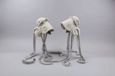 Two beaded pioneer bonnets sit facing each other on a gray background. The bonnets are white. Photo courtesy of UMFA. 