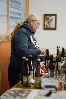 Torrence stands over several bottles of cider with a tool to open them. Photo: Em Behringer