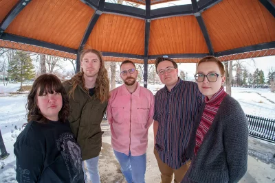 The members of Sharing stand semi-circle around the camera in a gazebo during winter. Photo: Chay Mosqueda