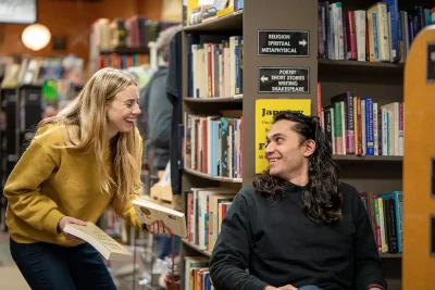 (L–R): Bri McCall and Danny Patiño exchange playful looks in a library. 