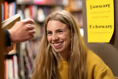 Bri McCall smiles in a library wearing a yellow sweater. She has long blonde hair.