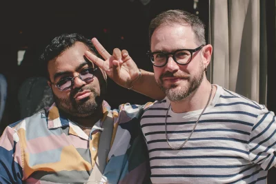 Photo of two people standing in front of garage door. The one on the left is holding up a peace sign.