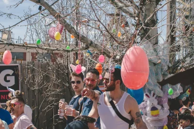 A group of people stand underneath a tree decorated with colorful hanging Easter eggs.