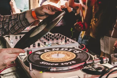 Picture of hands replacing a record on a turntable. The slipmat reads "RANDY'S-Since 1978"