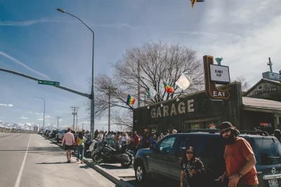 Picture of a group of people waiting outside of the venue. There is a car parked next to the crowd, along with a motorcycle.