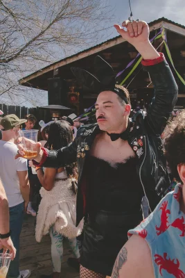 Person dancing at the event. They are wearing a short black dress, fishnets, a leather jacket with patches, and a pair of black bunny ears.