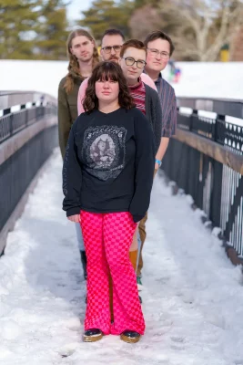 The members of Sharing stand in a single file line facing the camera, each one leaning out. They are standing on a snowy bridge. Photo: Chay Mosqueda