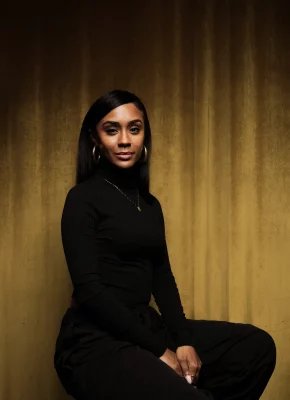 A.V. Rockwell sits against a gold backdrop wearing an all-black outfit. Photo courtesy of Focus Features. 