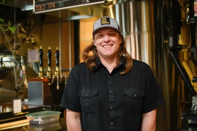 Grid City Brewmaster Jeremy Gross stands in Grid City in front of a brewing tank. 