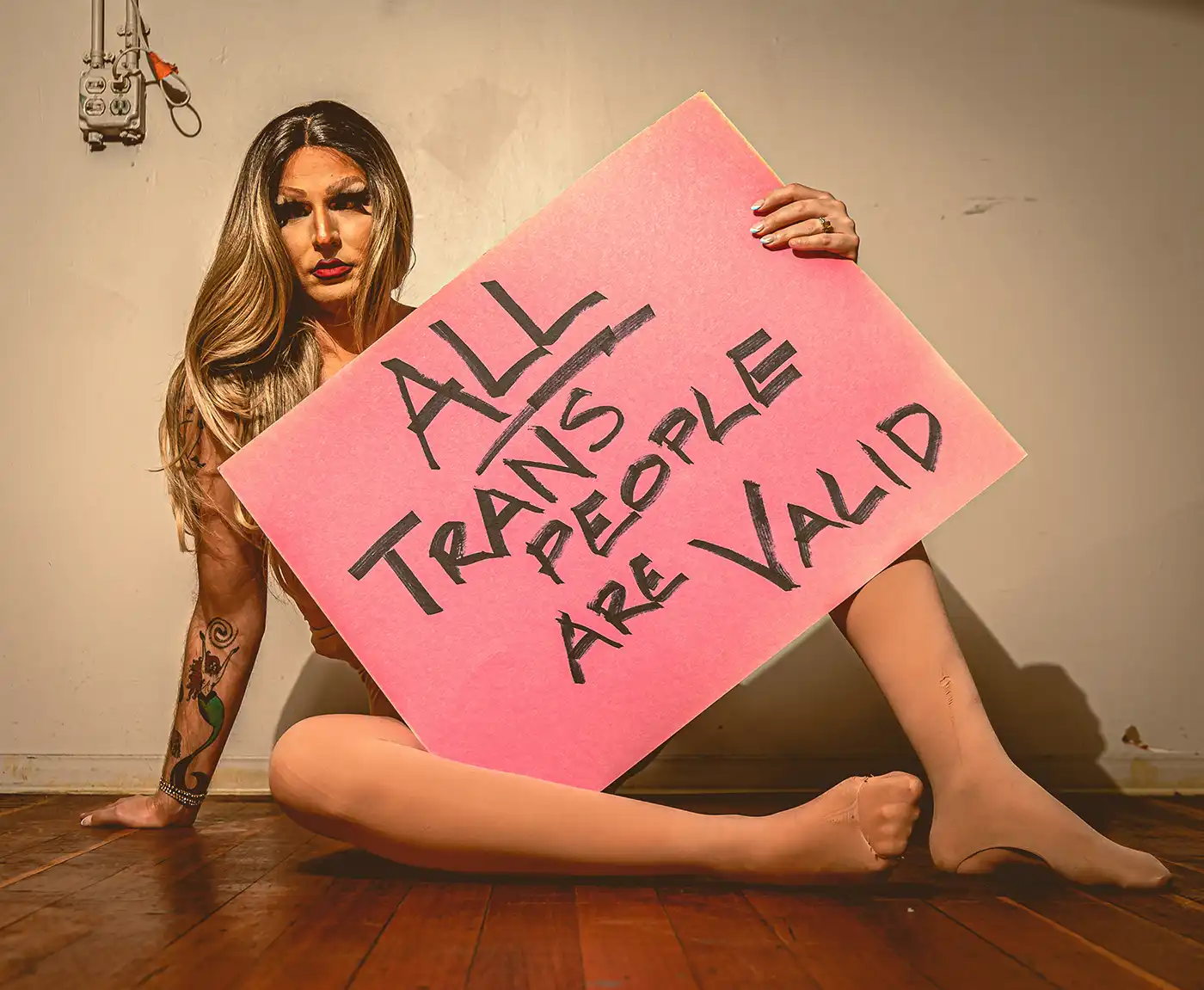 A woman sits with a sign that reads, "ALL trans people are valid."
