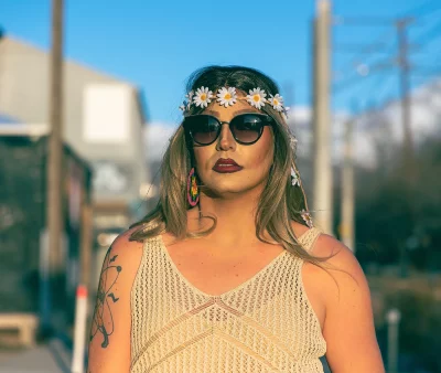 Photo of Drag Queen Tara Lipsyncki outside in a lace tank top, sunglasses and sporting a daisy crown.