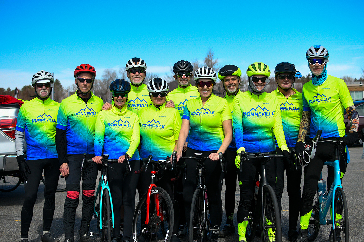 A group of Bonneville Cycling Club members stand in a group photo wearing bright, lime green and blue cycling shirts. Photo: Em Behringer