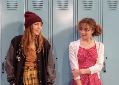 Two teens stand against a set of high school lockers. 