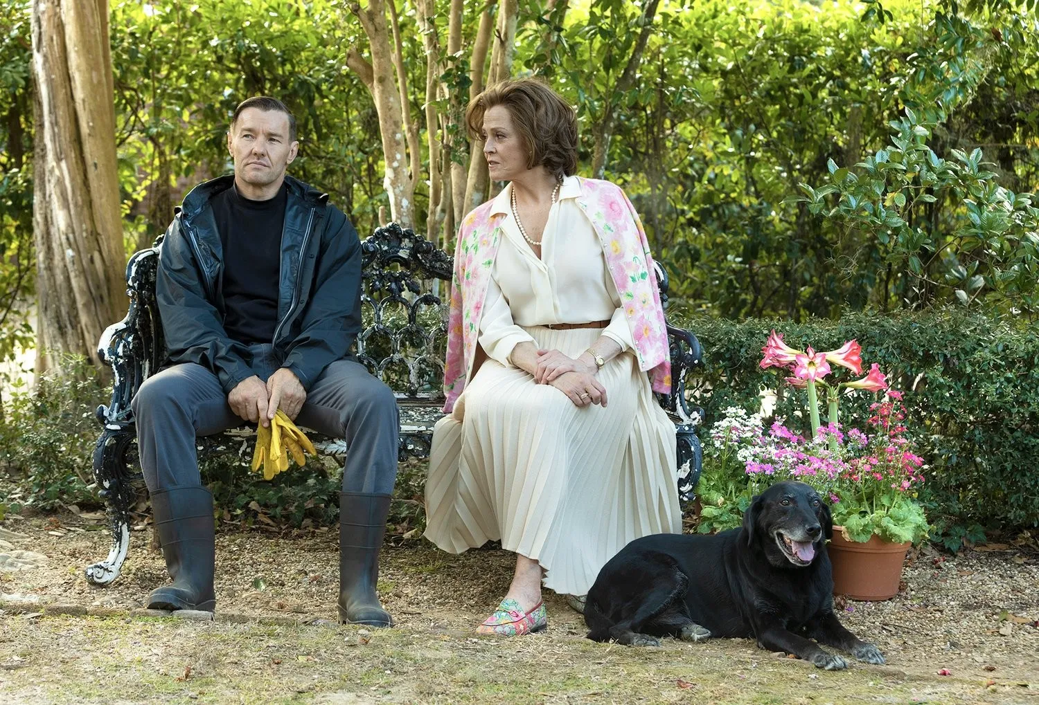 Two people sit together in a private garden. Next to them is a black dog.