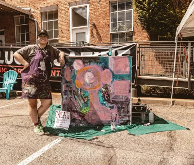 Artist Meau Brinky standing in front of a canvas they are currently painting.