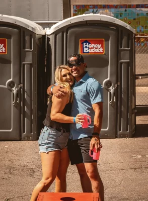 A couple posing in front of a group of porta-potties.