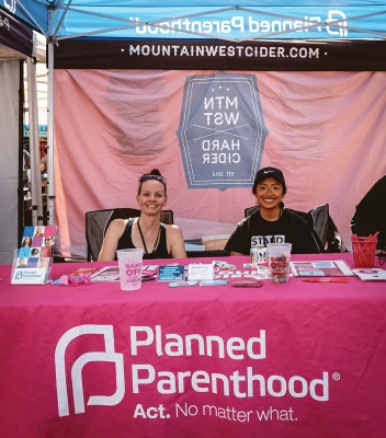 Two people sitting at the pink Planned Parenthood booth.