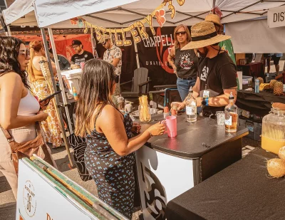 Two people working the Distillery 36 tent serving drinks to a customer.