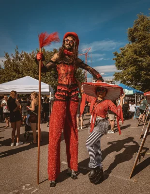 A person on stilts nexts to someone wearing a large hat.