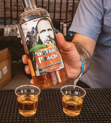 Two shotglasses of peach whiskey, with a person holding a bottle of peach whiskey.