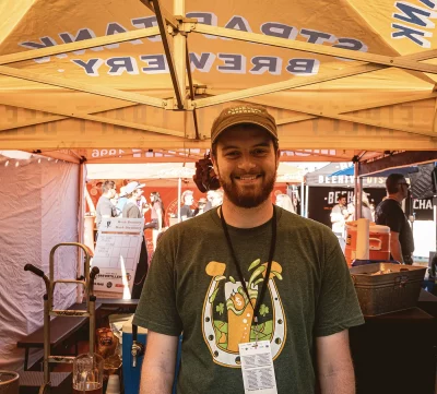 A person posing for a photo inside of the Strap Tank Brewing tent.