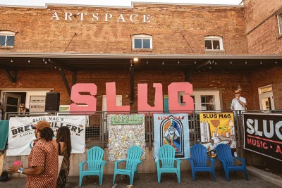 A collection of blue lawn chairs in front of the word "SLUG" In large pink letters.