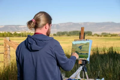 A participant in the Spring City Plein Air Competition stands outside with an easel and paints a Sanpete County landscape. Photo courtesy of Spring City Arts. 