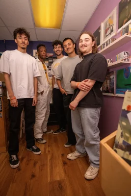All five members of CLUB MUNGO stand together inside a record shop.