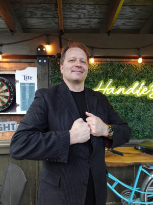 Jon Bean poses for the camera in a black pinstripe suit jacket at Handle Bar. 