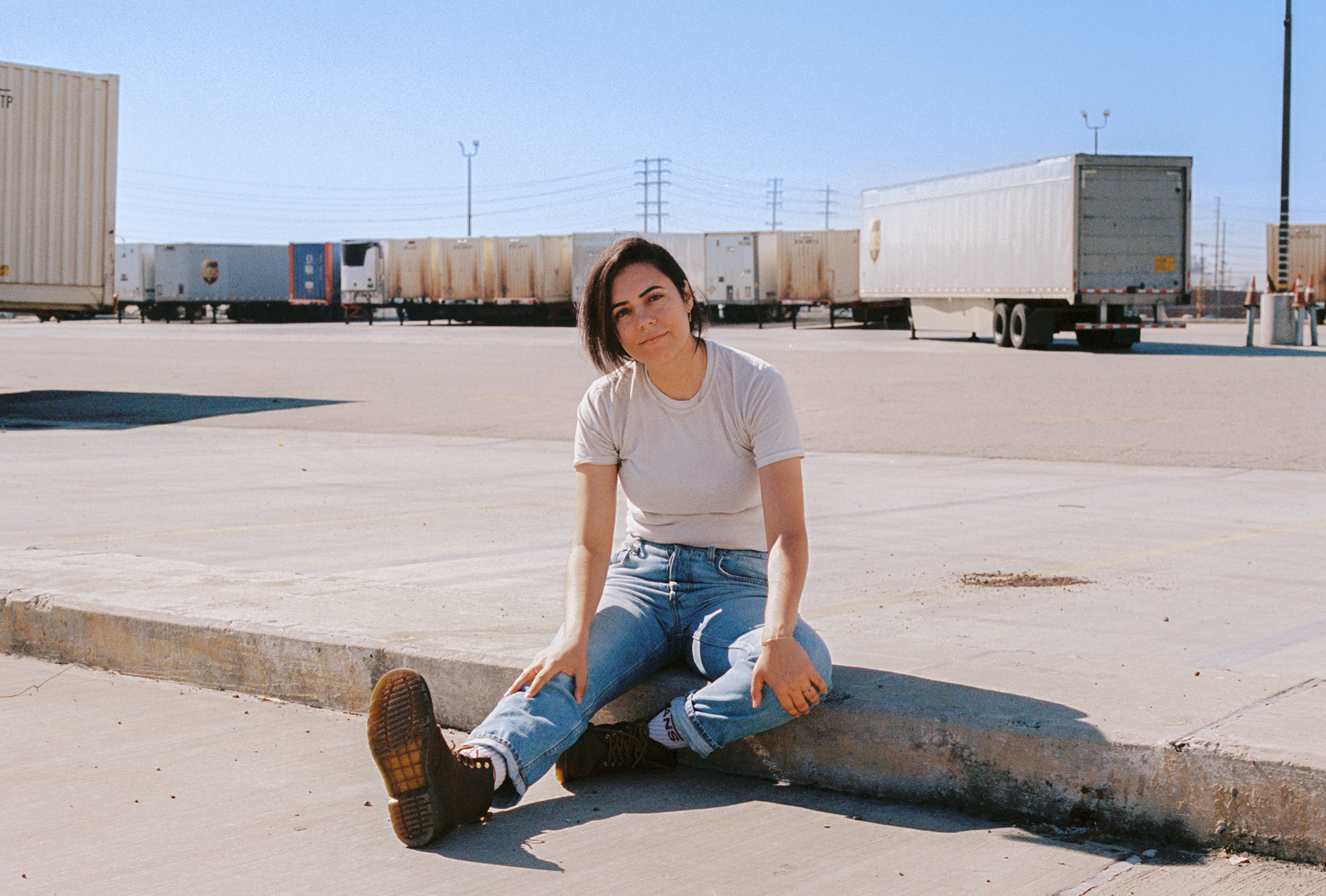 Songwriter-producer Sarah Tudzin of illuminati hotties sits on the ground in front of a train.