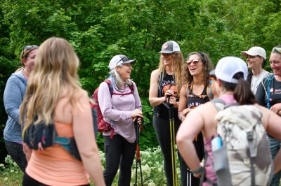Eight members of the Women's Wine Hiking Society gather and chat outdoors. 