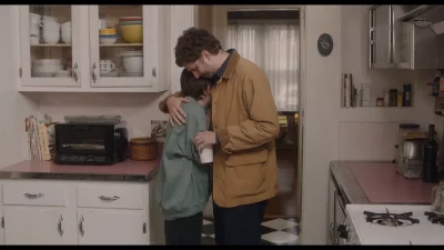 Actors Michael Cera and Sophia Lillis share an embrace in a kitchen.