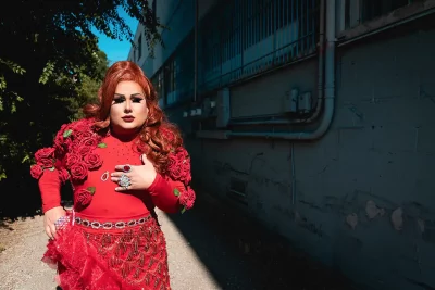 Lexis Monroig stands in front of an alleyway with a red, rose-adorned, fabulous dress. Photo: Bonneville Jones