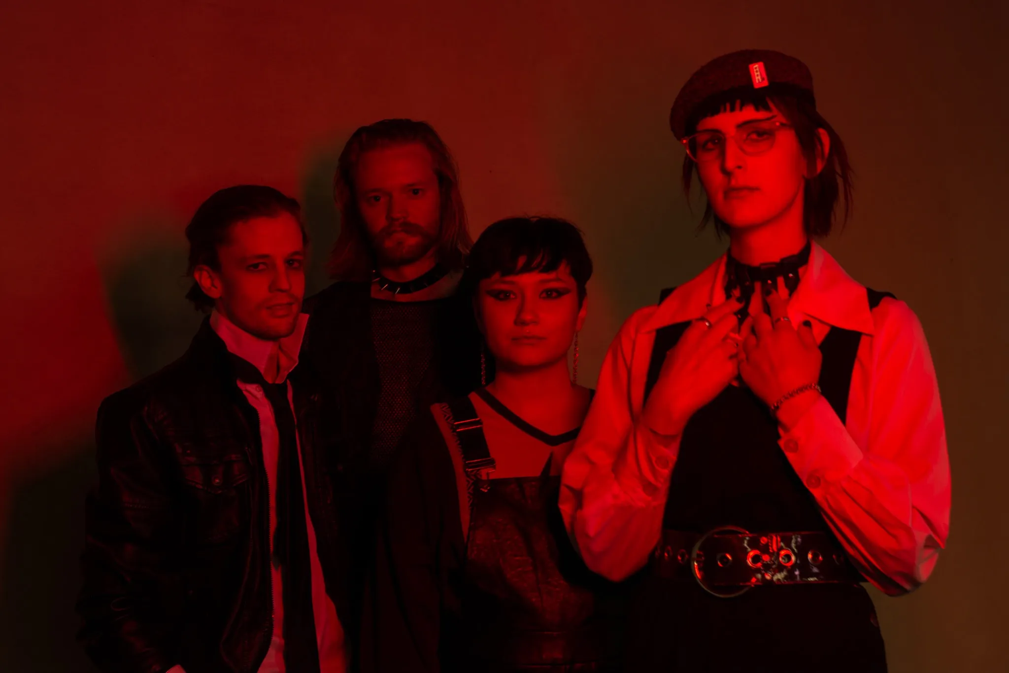 (L–R) Connor Collings, Dirk Jeffrey, Cecil Smith and Julie Boswell of Body Horror stand in a line under a dark red light.
