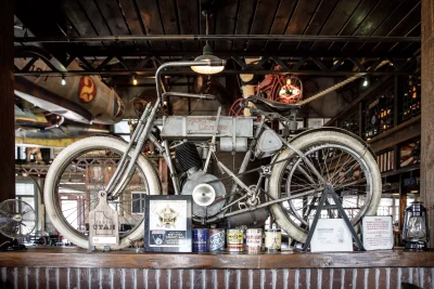 A old motorcycle is mounted on the wall above a bar area at Strap Tank Brewery.