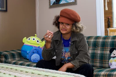 Katie sitting on a plaid couch with a stuffed animal, showing off a hand covered in rings.